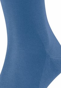 Calzino blu con caviglia realizzato in un tessuto liscio con una texture a coste e una costruzione senza cuciture, caratterizzato da una forma aderente che si adatta al piede.