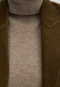 Brązowa marynarka z mieszanki wełny z klapami z wcięciami, noszona na beżowym golfie. Tkaniny mają miękką teksturę, a kolory są stonowane i ciepłe.