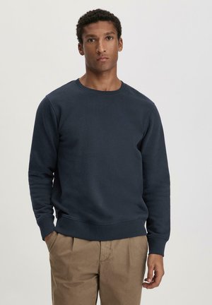 Marineblauwe crewneck sweatshirt van zachte stof, voorzien van geribbelde manchetten en zoom, gecombineerd met lichtgekleurde broek.