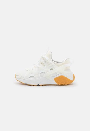 Biały sportowy sneaker z siateczkowymi i syntetycznymi nakładkami, białe sznurowadła oraz gumowa podeszwa z fakturowanym bieżnikiem, widoczny od zewnętrznej strony.