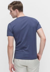 T-paita tummansinisestä pehmeästä kankaasta, lyhyet hihat, pyöreä kaula-aukko ja slim fit -malli, näkyy takaa.