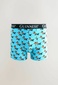 Helle blaue Boxershorts mit einem wiederkehrenden Tukan-Muster und einem schwarzen Bund mit dem Guinness-Logo in Weiß.