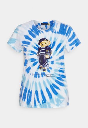 Sinivalkoinen batikkikuosinen t-paita, jossa karhu pukeutuneena laivastonsiniseen takkiin, raidalliseen paitaan, housuihin ja lippalakkkiin, jossa on teksti "Polo Bear by Ralph Lauren".
