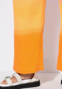 Oranje textuur wijde broek met een subtiele gradient zoom, gecombineerd met witte sandalen met een gestructureerde band en een zwarte plateauzool.