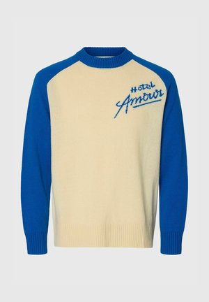 Pulover krem barve z modrimi rokavi in ovratnikom, na zgornjem levem delu prsi vezen napis "Hotel Amour".