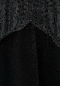 Černá tkanina s květinovým krajkovým lemem podél horního okraje, ukazující jemnou síťovinu a pevné tkaninové textury pod ní.