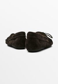 Brune loafers i ruskind med flad sål, prydet med en dekorativ rem og samling bagpå. Blød tekstur og afrundet form.