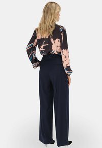 Czarna bluzka w kwiaty z różowymi i niebieskimi wzorami, zestawiona z granatowymi spodniami o szerokich nogawkach i wysokim stanie, gładki materiał, luźny krój.