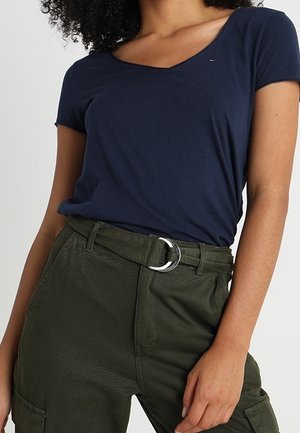 Navyblauwe, kortekorte mouw t-shirt met V-hals, gecombineerd met olijfgroene, getextureerde, hooggetailleerde broek met een zilveren, ronde riemgesp.