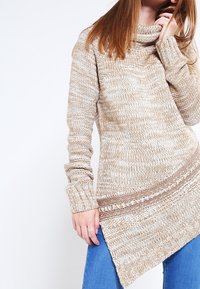 Beżowy sweter dziergany z golfem, teksturowanymi wzorami i ukośnym wykończeniem. Posiada długie rękawy i luźny fason.