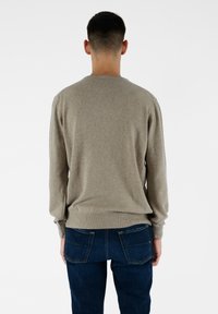 Beżowy sweter dzianinowy z okrągłym dekoltem, ściągaczami na mankietach i na pasie. Połączony z ciemnoniebieskimi dżinsami z podwójnymi tylnymi kieszeniami.