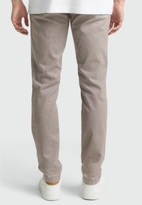 Lichtbruine tapered broek van gestructureerde stof, voorzien van een elastische zoom en gedragen met witte sneakers.