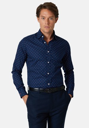 Granatowa koszula na guziki z małym czerwonym geometrycznym wzorem. Wykonana z gładkiej tkaniny, posiada usztywniany kołnierz i mankiety na guziki.