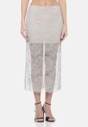 Femme portant une jupe midi en dentelle florale gris clair avec une doublure unie au-dessus des genoux et une dentelle transparente en dessous, associée à des talons noirs.