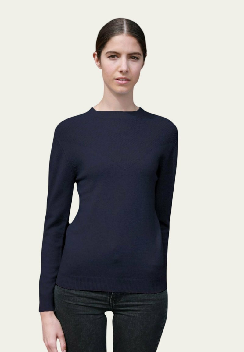 Pull à manches longues bleu marine avec un col rond, fabriqué dans un tissu lisse. Porté sur un jean foncé, avec une silhouette ajustée.