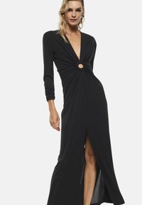 Abito maxi nero con maniche lunghe, scollatura a V profonda, frontale arricciato con un taglio circolare e uno spacco alto fino alla coscia. Realizzato in materiale morbido e elastico.