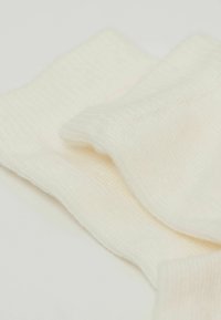 Cremefarbener geripptes Textil mit einer weichen Textur. Mehrere leicht überlappende Lagen, um Materialdetails und Design zu zeigen.