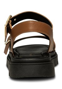 Hnědá kožená sandál s dvěma vodorovnými pásky a přezkou, s tlustou černou gumovou podrážkou s texturovaným dnem.