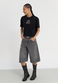 Black short-sleeve cropped t-shirt with multicolored embroidered text, paired with high-waisted gray denim culottes and knee-high black boots.