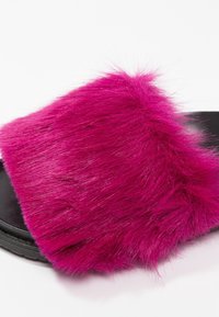 Sandale slide en fourrure fuchsia avec une texture moelleuse et une large bride, dotée d'une semelle noire pour le contraste et la durabilité.