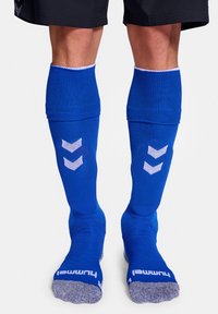 Blauwe sportkousen met een gebreide textuur, voorzien van witte chevronpatronen op de kuiten en contrasterende grijze accenten op de zolen.