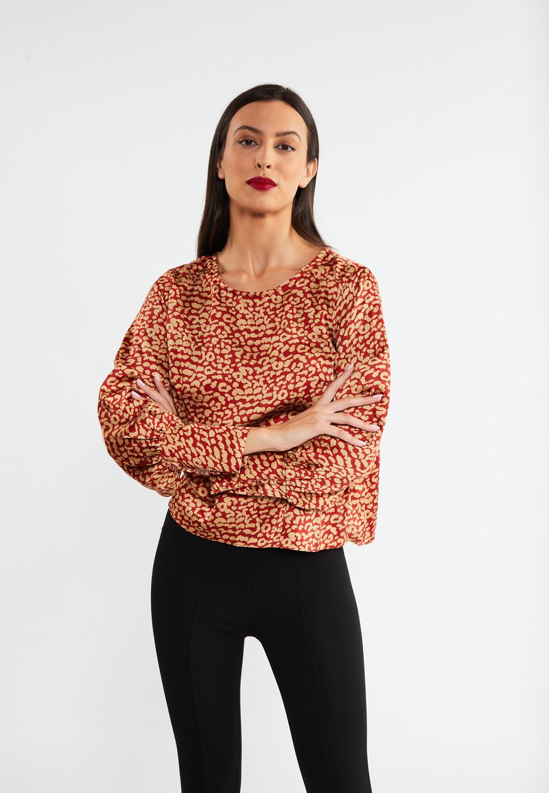 Rood en gouden blouse met patroon, ronde halslijn, volumineuze mouwen, gecombineerd met zwarte leggings. Glad materiaal, ontspannen pasvorm, casual ontwerp.