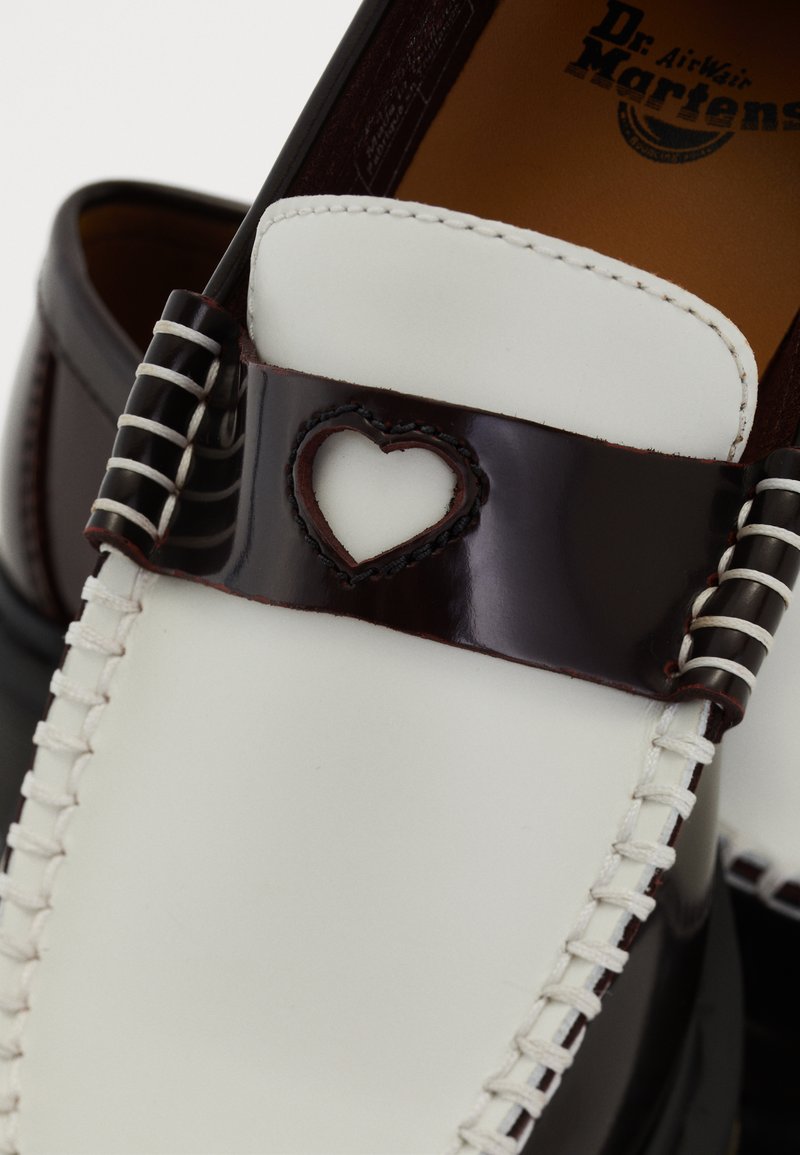 Mocassin en cuir blanc avec une bande marron foncé dotée d'une découpe en forme de cœur et d'une couture blanche visible, semelle intérieure de marque Dr. Martens.