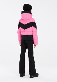 Veste en duvet avec un corps rose, des accents en chevron noir, une capuche et une ourlet côtelé. Stylisée avec un pantalon texturé noir et des bottes noires épaisses.