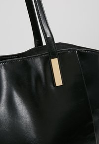 Black leather handbag with stitched handles and a rectangular gold metal accent on the strap near the bag opening.