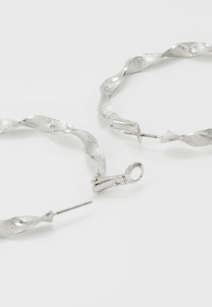 Boucles d’oreilles créoles torsadées en argent avec surfaces alternées texturées et lisses, dotées de fermoirs à clapet sur fond blanc.