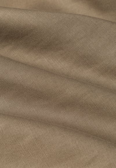 Tessuto beige con una superficie liscia, che mostra un motivo di trama costante e un leggero luccichio, piegato per mostrare profondità e dimensione.