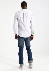 Camisa de manga larga gris claro con un pliegue en la espalda, puños con botones, combinada con unos vaqueros azul oscuro y zapatillas altas grises con una franja.