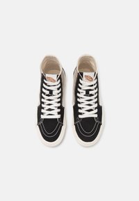Svarta högre sneakers av kanvas med vita snören, krämfärgade detaljer och synliga sömmar. Har en logotagg på tungan och en rundad tå.