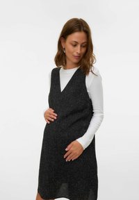 Juoda tekstūruota suknelė su V formos iškirpte, dėvima virš baltos ilgomis rankovėmis marškinėlių, tinkama nėštumui. Lygi, laisvalaikio medžiaga.