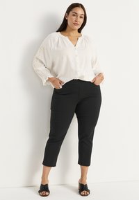 Witte blouse met knoopsluiting en geborduurde mouwen, gecombineerd met zwarte cropped broeken en zwarte instap-sandalen. Gladde stof, ontspannen pasvorm.