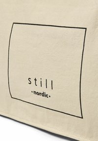 Beige Stofftasche mit schwarzem rechteckigem Rahmen und minimalistischer Textgestaltung mit der Aufschrift "still nordic." Glatte Textur.