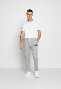 Grå sweatpants med snor i taljen og logo på venstre lår, parret med en simpel hvid t-shirt med rund hals og hvide sneakers.