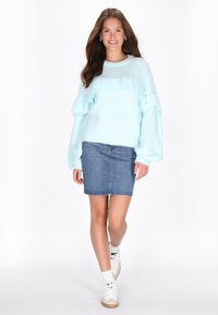 Jasnoniebieski puszysty sweter z falbaniastymi detalami, połączony z dżinsową spódnicą i białymi trampkami. Miękka faktura i swobodny design.