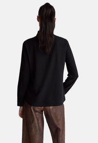 Czarna bluzka z długim rękawem o luźnym kroju, charakteryzująca się gładką fakturą i mankietami na guziki, zestawiona z błyszczącymi, szerokimi spodniami w kolorze brązowego brązu.