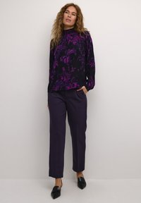 Haut à manches longues noir avec un motif floral violet associé à un pantalon violet taille haute et ample, et des mocassins noirs à bout pointu.