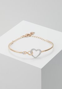 Gold-tone metal bracelet featuring an infinity symbol and heart design, adorned with clear cubic zirconia accents and a lobster clasp closure.