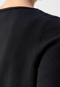 Maglione nero in maglia con scollatura rotonda e tessuto a trama. Il primo piano mostra la superficie liscia e i dettagli delle cuciture sulla spalla.