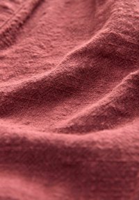 Textured fabric in a muted reddish-brown color, displaying soft, wrinkled folds with a slightly uneven surface.