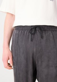 Pantalon en tissu doux de couleur grise avec une taille élastique et un cordon de serrage. Présente des poches latérales et une coupe décontractée, idéale pour une tenue de tous les jours.