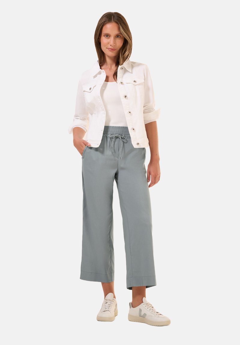 Giacca in denim bianco, pantaloni grigi chiari a vita elastica e sneakers beige. Design semplice, vestibilità casual.