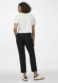 Weißes, kurzes T-Shirt, schwarze, maßgeschneiderte Hose und weiße Sneaker mit schwarzen Akzenten. Der Stoff wirkt glatt; die Hose hat Gesäßtaschen.