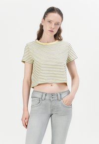 Stripet topp i gul og marineblått, kortermet, rund hals. Kombinert med lys grå jeans som har dobbel knappelukking og sidelommer.