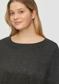 Zwarte sweatshirt met een textuur en een ronde halslijn, met subtiele spikkels van een lichtere kleur door de stof heen.