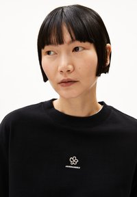 Zwarte sweatshirt met een ronde hals, voorzien van een klein wit geborduurd bloemenlogo op de borst. Glad materiaal en een ontspannen pasvorm.