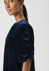 Top din catifea bleumarin, cu mâneci puff strânse, textură netedă și decolteu rotund, evidențiind o siluetă elegantă.